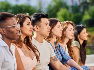 Group of multiracial young people looking away while sitting in row together outdoors. Team and unity concept.
