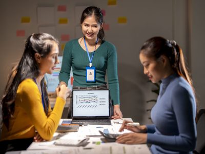 Three women are sitting at a table with a laptop open in front of them